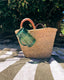 Woven bag with a green sippy cup on a striped towel under a tree swiggee