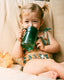Child in a swimsuit holding a green sippy cup on a beige couch