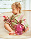 Child wrapped in a pink and green towel sitting on a chair with a pink sippy cup. swiggee